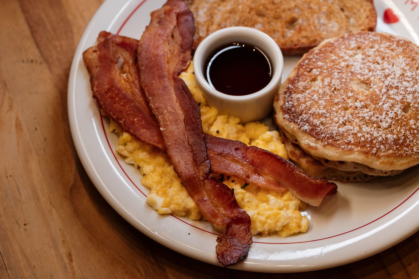 A brunch plate with scrambled eggs, bacon, pancakes and maple syrup